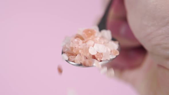 Full metal spoon of rough Himalayan salt on pink background in hand. Falling mineral seasoning