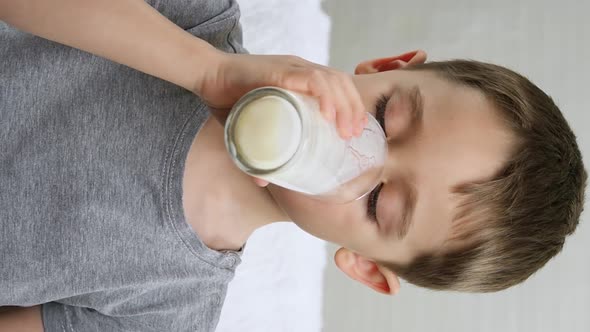 A Charming Little Boy Drinks Yogurt, Milk From a Glass Cup. Health Food. Vertical Video