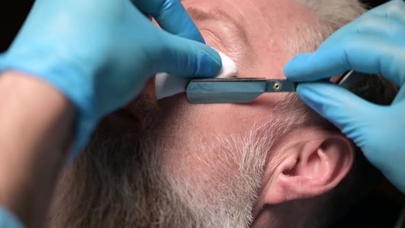 Barber correcting beard of an adult man, close-up. Working with a straight razor