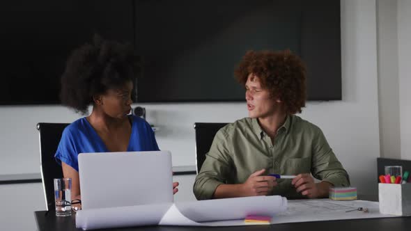 Diverse male and female business colleagues in discussion at work using laptop computer