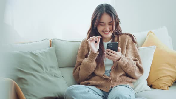 Happy young asian woman surfing social media on mobile phone, enjoying amazing news