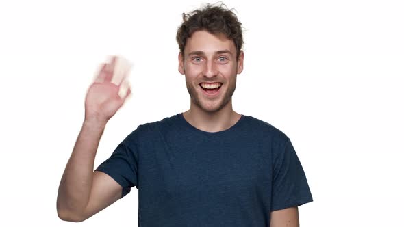 Portrait of Smiling Young Man Greeting with Waving Hand on Camera Isolated Over White Background in