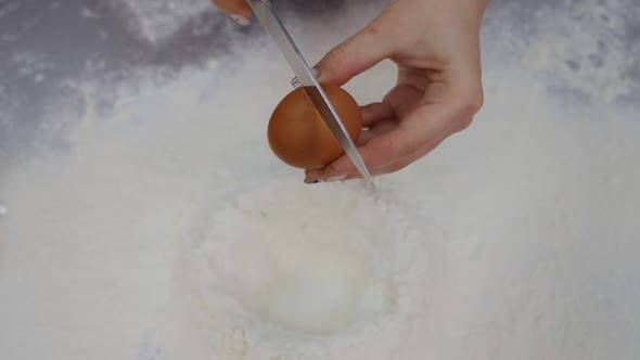 Closeup of a Cook Breaking an Egg Into Flour on a Table in a Pastry Kitchen
