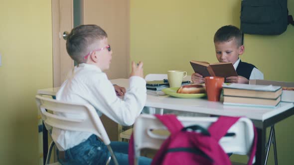 Boy Play with Pen Schoolmate Reads Book at Table in Canteen