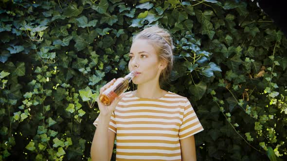 Woman drinking lemonade in front of ivy wall