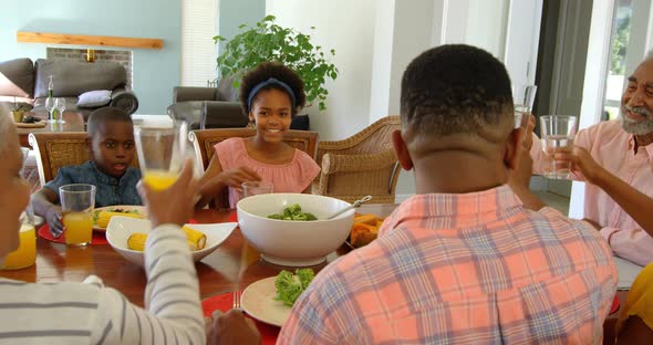 Happy mixed race multi-generation family toasting glasses of juice at dining table at home 4k