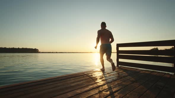 A Young Man is Running Down the Pier and Jumping Into the Lake in the Style of a Bomb