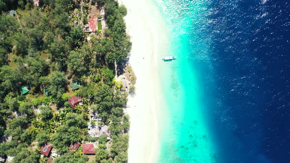 Tranquil tourist village with houses under tropical trees, in front of white sand of exotic beach an