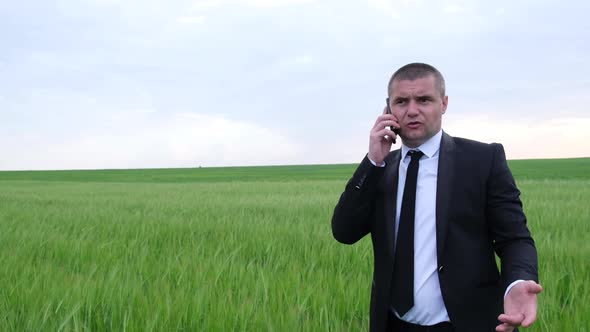 Angry Businessman Talking on a Smartphone in the Middle of the Field