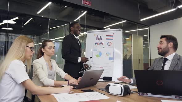 Businessman Joking During Flip Chart Presentation with Pleasant Smiling Business Partners