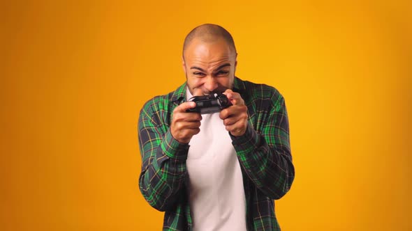 Young African American Man Playing Video Games with Joystick in Hands Against Yellow Background