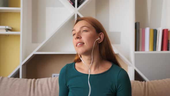 Calm Happy Young Woman in Headphones Chilling Sitting on Sofa Listening To Favorite Music