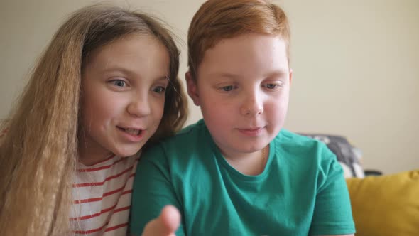 Joyful Small Boy and Girl Watch a Funny Video on Smartphone Sitting on the Sofa at Room