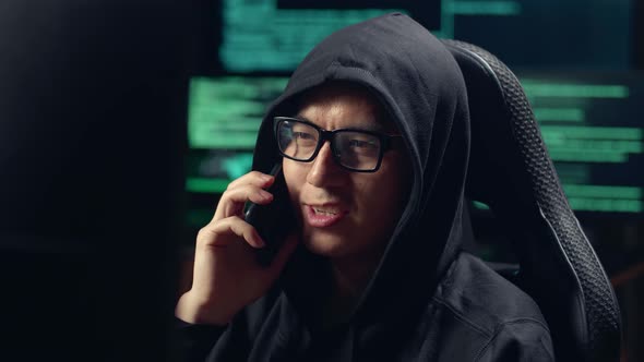 Asian Male Hacker Using Computer Hacking And Talking On Phone