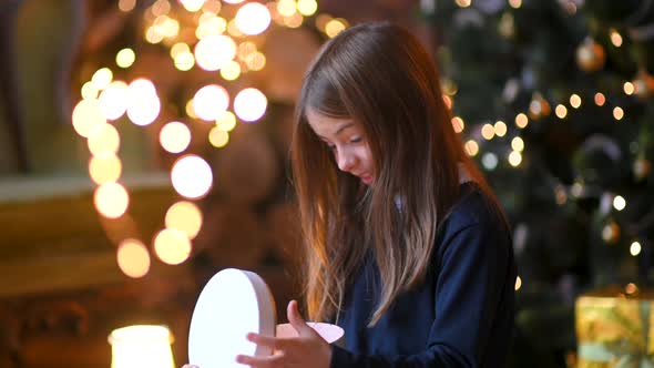 cute little girl sitting on the floor near the Christmas tree opens gifts