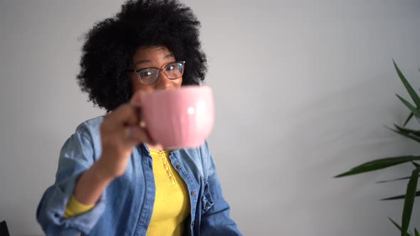 Laughing black female using smartphone and drinking cup of coffee