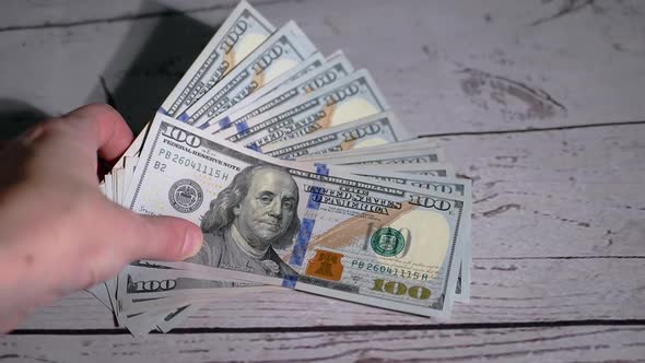 Female Hand Takes a Stack of Fanned Out 100 Dollar Bills Lying on the Table