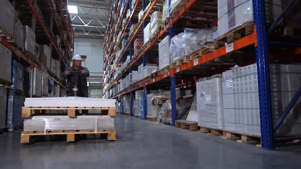 A Warehouse Worker Carries Huge Boxes on a Manual Forklift