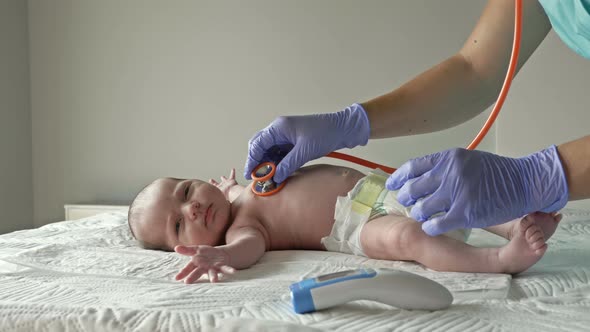 Neonatologist in Latex Gloves Examines a Newborn Baby with a Stethoscope