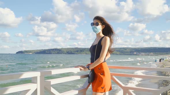 Fit Woman with Sunglasses and Face Mask Looking Over a Fence at the Sea. Protection Measures During