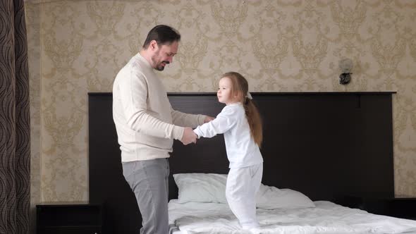 Happy Family Child Daughter and Dad Holding Hands Jumping on Bed