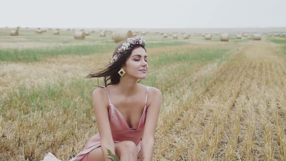 Elegant Lady in Dress with Flowers Sitting on a Stubble in Field and Posing