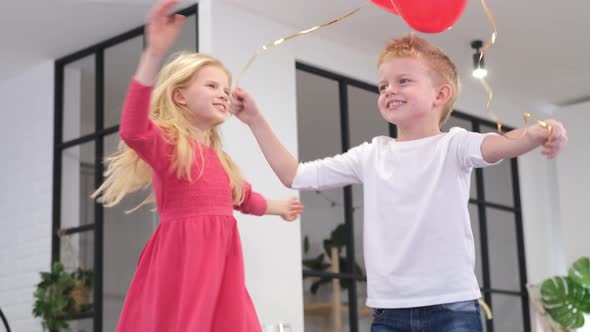 Little Boy and Girl Dancing with Red Heart Shape Balloons at Home