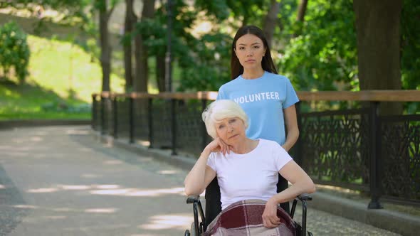 Upset Old Lady in Wheelchair and Sad Volunteer Looking Camera Outdoors, Hospice