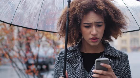 African American Woman Curly Girl with Transparent Umbrella Stands on Autumn Street in Rain Looks at