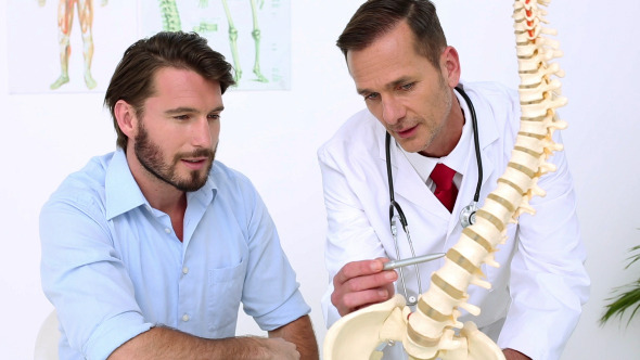 Patient Listening To Doctor Explain Spine Model