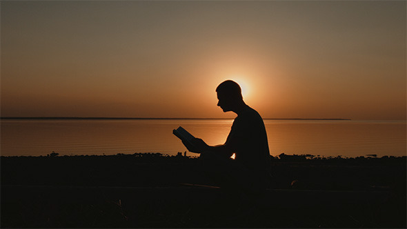 Man Reading a Book at Sunset on the Lake