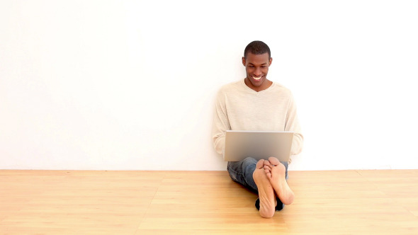 Smiling Man Using Laptop Sitting On The Floor alt