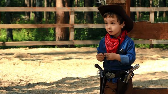 Little Cowboy Standing Near A Wooden Fence