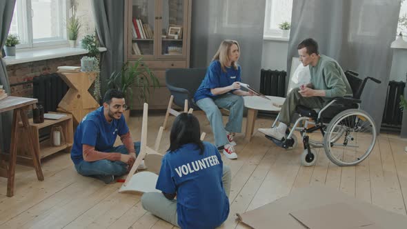 Group of Volunteers Assembling Furniture for Man in Wheelchair