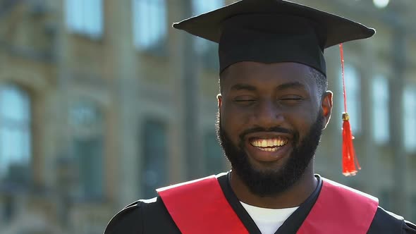 Proud Afro-American Student in Hat and Gown Looking to Camera and Smiling