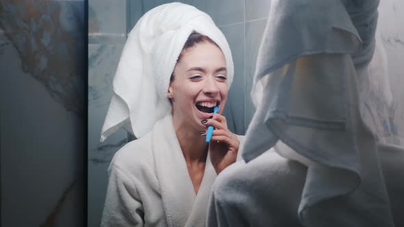 Young Beautiful Woman in the Bathroom Brushing Her Teeth in Front of the Mirror