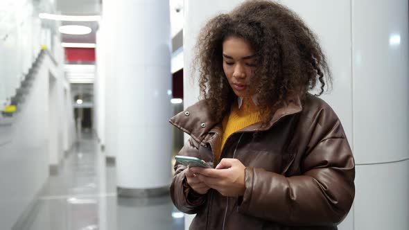 African Female Waits for a Train in the Subway and Uses a Smartphone Surfs the Internet a Young