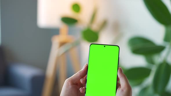 Woman at Home Using Smartphone with Green Mockup Screen in Vertical Mode