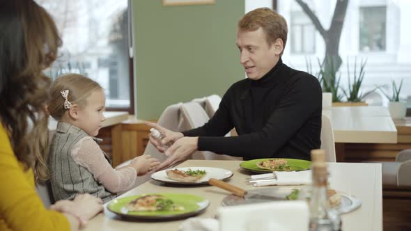 Positive Caucasian Man Spraying Sanitizer on Hands of Wife and Daughter in Pizzeria