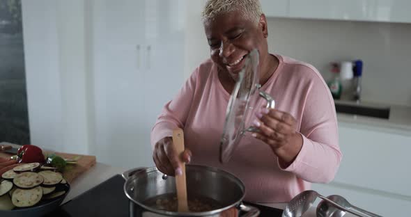 Happy black senior woman cooking lunch inside kitchen