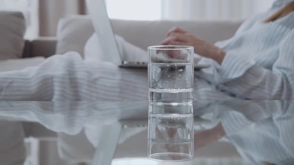 Glass of Iced Water on Table on the Background of a Woman with a Computer