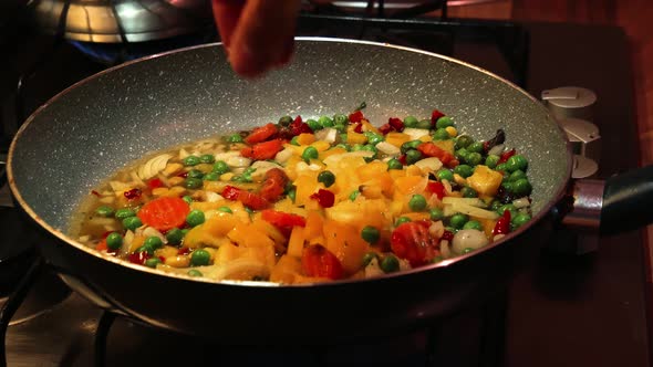 Homemade chef hands seasoning fresh vegetables in the pan. Hot oil. Salt.