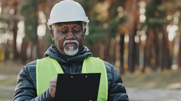 Mature Concentrated Forestry Engineer Technician Forester in Protective Helmet Stands in Park