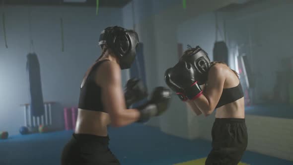 Combat Sparring of Two Females Fighters Wearing Protective Helmets Training in the Boxing Gym