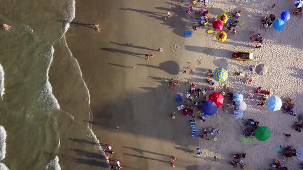 Aerial top down shot flying over people enjoying a beautiful beach at golden hour. Dolly out