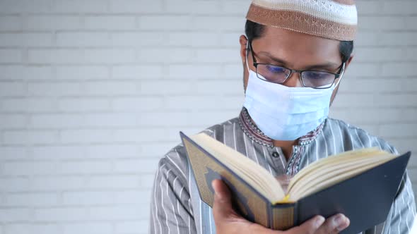 Muslim Man with Face Mask Reading Holy Book of Quran alt