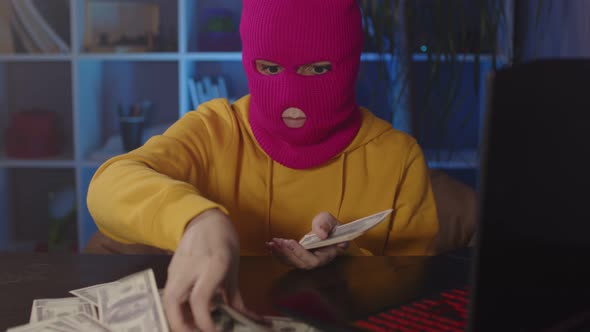 Young Woman in Pink Balaclava Collects Money From Table in Office