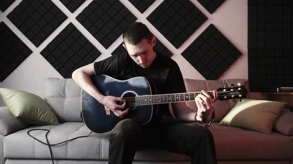 Young Man Playing Acoustic Guitar While Sitting on Sofa in Home Recording Studio