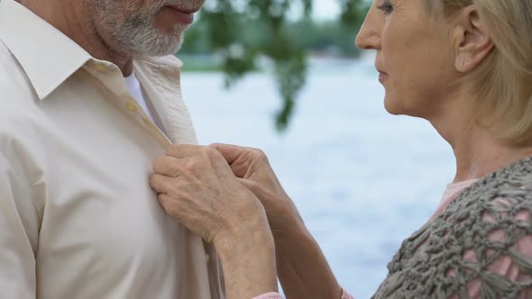 Mature Man Looking With Love and Tenderness, Caring Woman Buttoning His Shirt