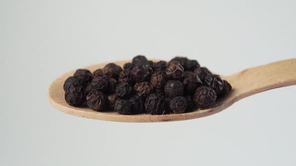 Black peppercorns in a wooden spoon. Falling black pepper seeds